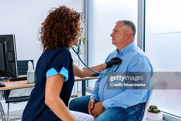 doctora usando un estetoscopio y escuchando a un paciente masculino en un consultorio médico - obesidad fotografías e imágenes de stock