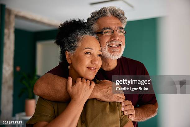 happy senior couple embracing and looking away at home - medelålders bildbanksfoton och bilder
