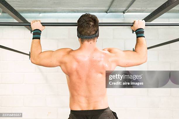 muscular athlete doing pull-ups in a gym - pull ups stock pictures, royalty-free photos & images