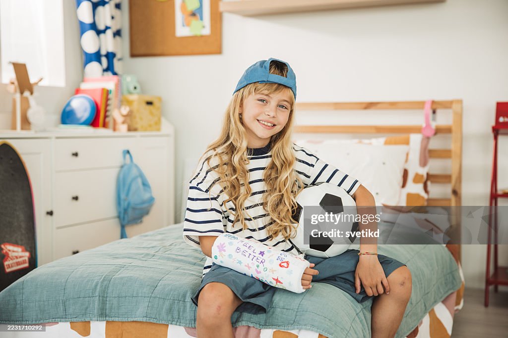 Süßes Mädchen mit Fußball und gebrochenem Arm im orthopädischen Gips