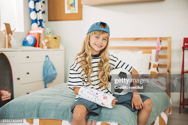 süßes mädchen mit fußball und gebrochenem arm im orthopädischen gips - gebrochener arm stock-fotos und bilder