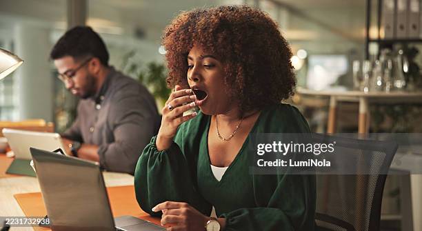 mujer profesional cansada bostezando durante un día ajetreado en la oficina moderna - bostezar fotografías e imágenes de stock
