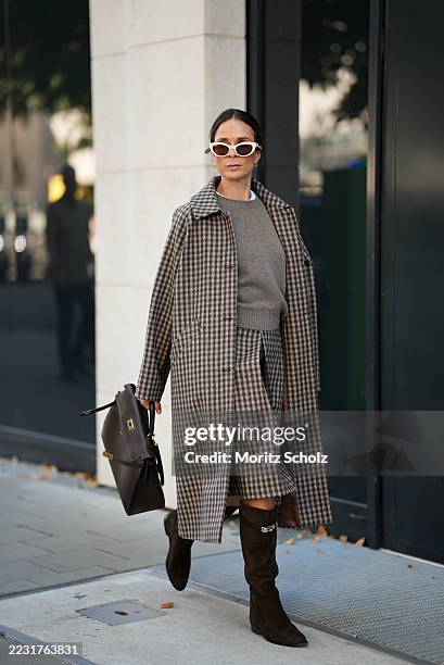 Patricia Wirschke is seen wearing a checked beige and brown long trench coat paired with a knee length tiered skirt of the same pattern; a greige...