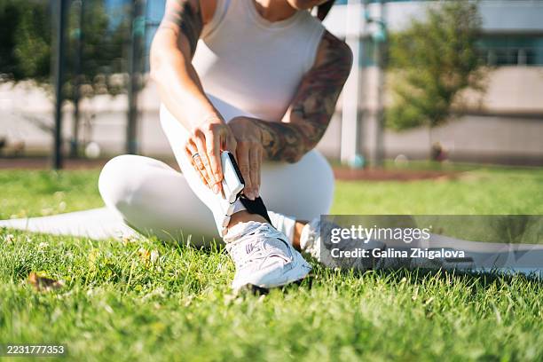 athletic woman putting on ankle weights on yoga mat at outdoor gym - ankle weights stock pictures, royalty-free photos & images