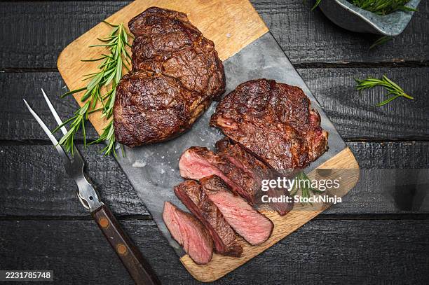 delicious grilled ribeye steak served on wooden cutting board with rosemary - rib eye steak stock pictures, royalty-free photos & images