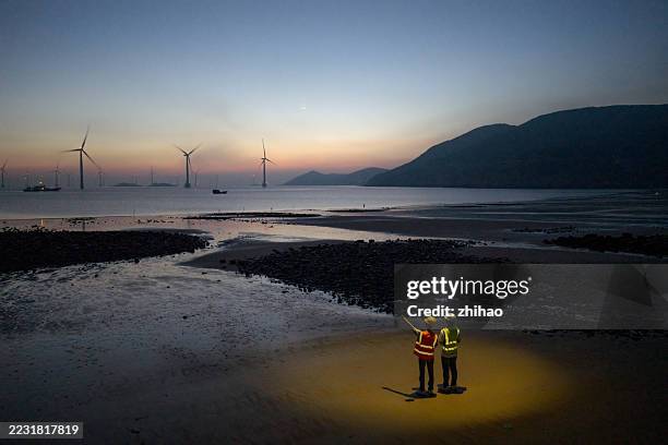 on the beach at dawn, the wind farm technicians are at work - neutralité carbone photos et images de collection