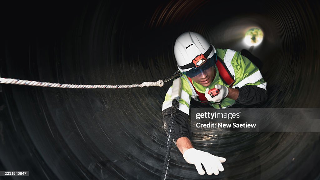 Workers operate inside a massive steel pipeline, constructing infrastructure for oil, gas, and fuel at a bustling industrial site.