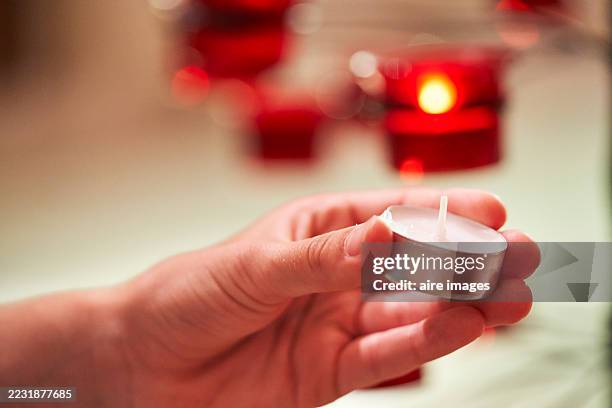 hand holding a small tea light candle with red candle lights in the background - tealight stock pictures, royalty-free photos & images