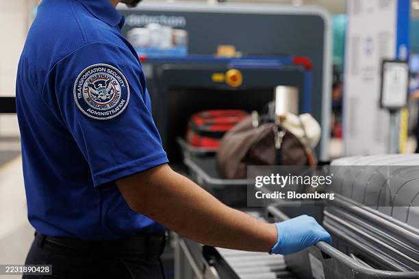 Transportation Security Administration agent monitors travelers as they place their luggage onto a scanner belt at the TSA security checkpoint at...