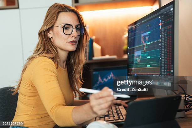 eine frau beobachtet den handel mit krypto-charts zu hause aufmerksam - finanzberuf stock-fotos und bilder