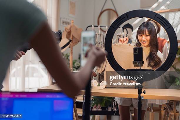 asiatische influencerin streamt mode live und verkauft damenbekleidung und taschen mit produktionsteam im heimstudio. die einrichtung mehrerer kameras zeigt social commerce durch authentische markenpartnerschaften und echtzeit-engagement für den omnichann - botschafter stock-fotos und bilder