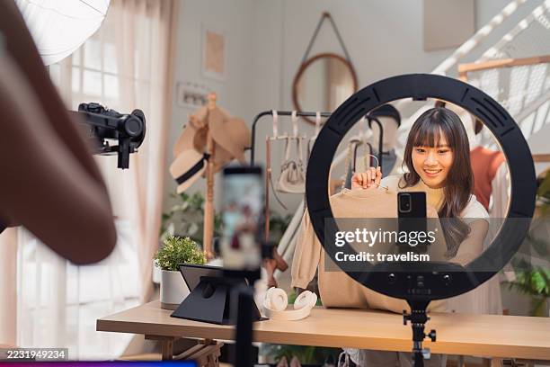 asiatische influencerin streamt mode live und verkauft damenbekleidung und taschen mit produktionsteam im heimstudio. die einrichtung mehrerer kameras zeigt social commerce durch authentische markenpartnerschaften und echtzeit-engagement für den omnichann - botschafter stock-fotos und bilder