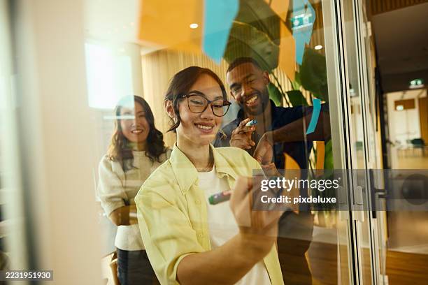 young businesswoman writing on glass wall during brainstorming session with coworkers - project management stock pictures, royalty-free photos & images