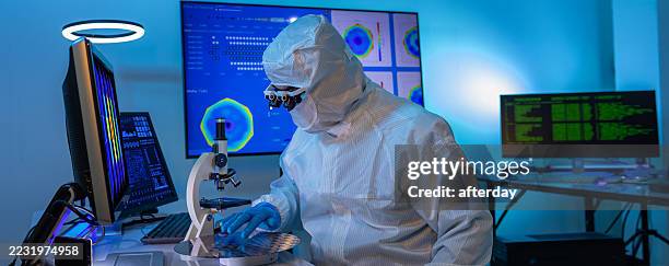 semiconductor production at electronics manufacturing facility. worker or engineer wears medical protective suit or white coverall suit with silicon wafer. - wafer stock pictures, royalty-free photos & images