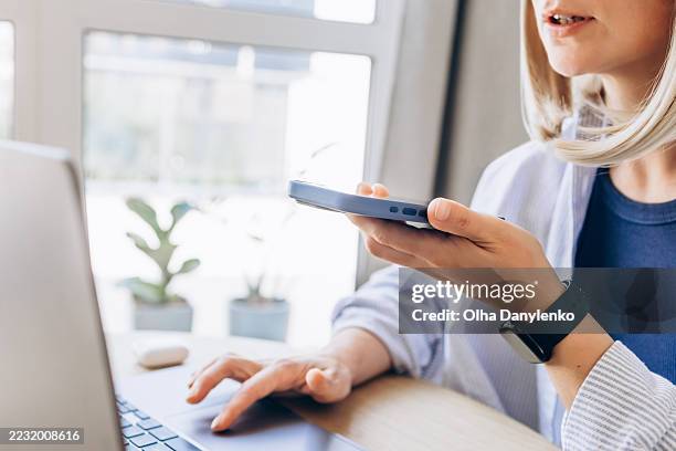 close-up of a person multitasking at a desk, speaking into ai chat while working on a laptop - vertaling stockfoto's en -beelden