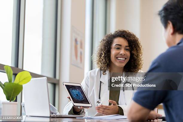 happy female doctor showing brain scan to patient - neurologist stock pictures, royalty-free photos & images