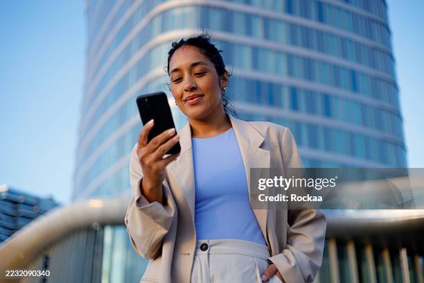 professional businesswoman texting on smartphone, standing near contemporary glass office tower, embodying corporate achievement - electronic banking stock pictures, royalty-free photos & images