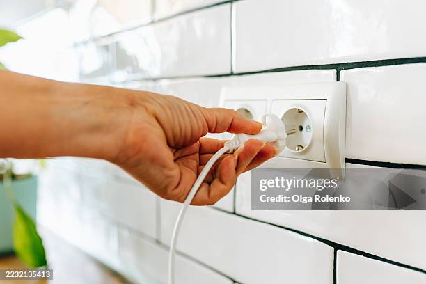 hand plugging a white electric plug into a socket on a tile wall - prise électrique photos et images de collection