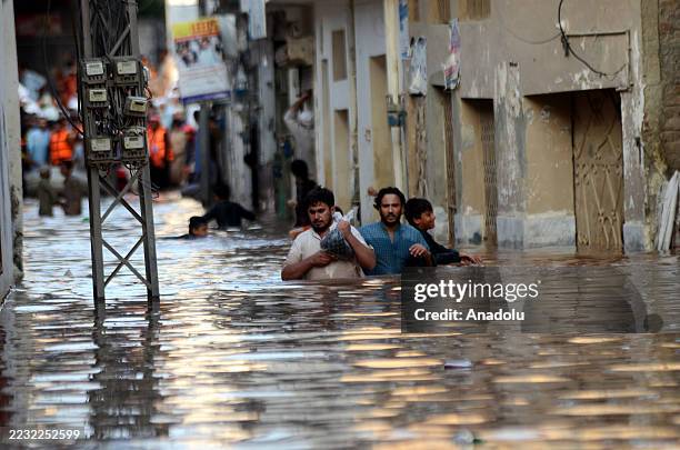 Residents, including children, wade through floodwater in a neighborhood along Charsadda Road after heavy rainfall triggered severe flooding,...