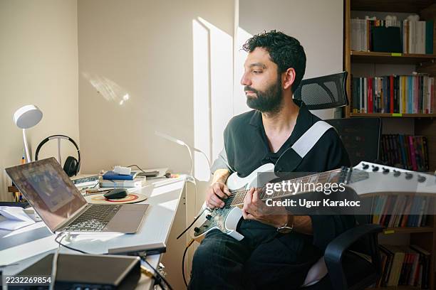 man with electric guitar looking at laptop screen with lesson open, practicing chords. concept of online education and distance learning. - liedjesschrijver stockfoto's en -beelden