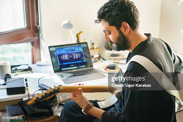 man practicing guitar at desk with laptop in background - songwriter stock pictures, royalty-free photos & images