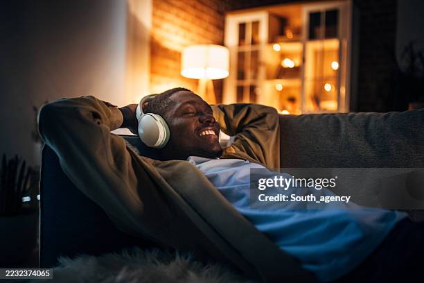 young black man relaxes at home while listening to music at night - ambient light stock pictures, royalty-free photos & images