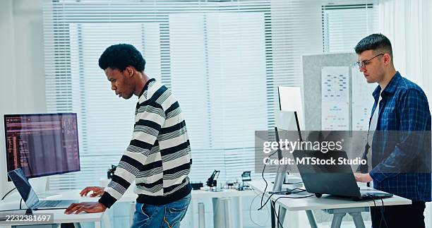 two male software developers analyzing data coding and working on multiple screens standing at desk in office. artificial intelligence and programming. - java code stock pictures, royalty-free photos & images