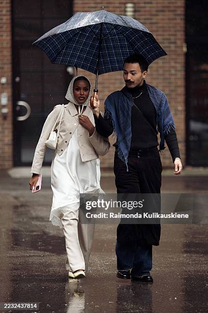 Guest wears beige pants, white dress, beige jacket and white head scarf and a guest wears navy blue jeans, black long sleeve top and blue scarf on...
