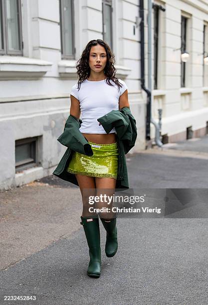 Seline Pettersen wears white cropped shirt, green sequined mini skirt, jacket, Hunter rain gum boots during Oslo Fashion Week on August 27, 2025 in...