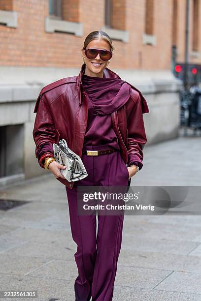 Nina Sandbech wears oversized burgundy leather jacket, blouse with scarf piece, pants, black white snake print bag, bracelets, sunglasses during Oslo...