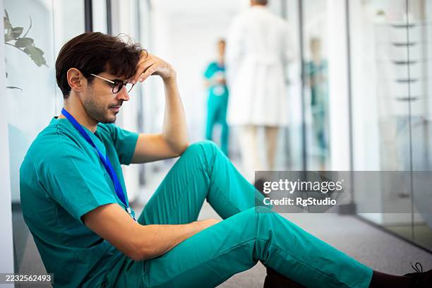 erschöpfter chirurg sitzt nach der operation auf dem krankenhausboden - laubsäge stock-fotos und bilder