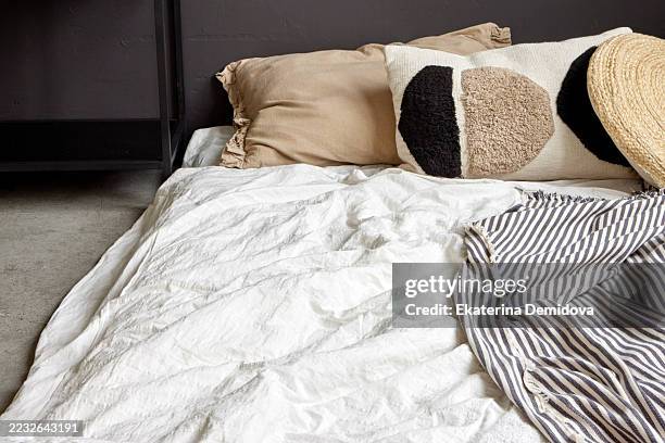 unmade bed with decorative pillows and striped blanket in modern bedroom - nordic countries stock pictures, royalty-free photos & images