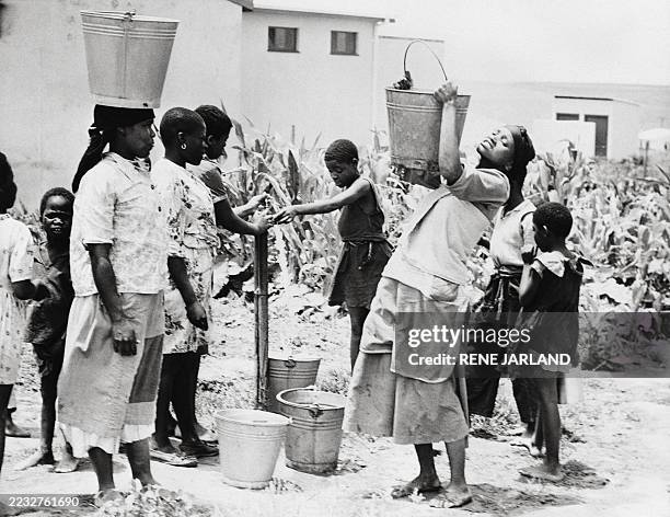 Dated photo from February 1963 of residents filling water buckets at a water source in a South African village.