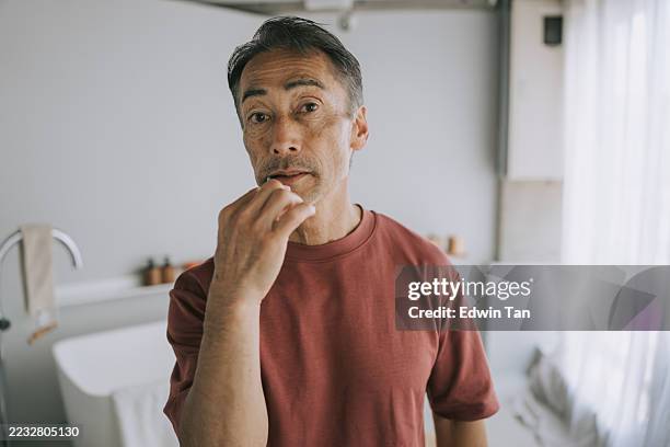 japanese senior man interacting with smart mirror while brushing teeth - old man brushing teeth stock pictures, royalty-free photos & images