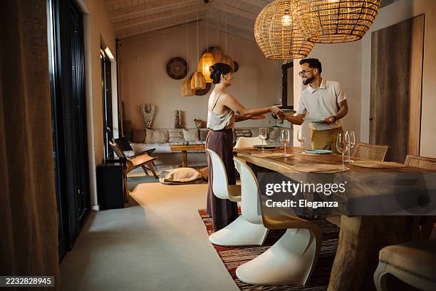 couple decorating dinner table while preparing to host friends - couple making dinner stock pictures, royalty-free photos & images