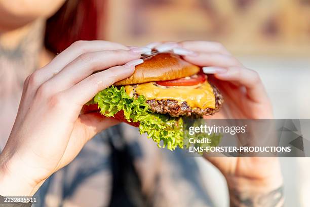 woman holds freshly made cheeseburger outdoors in the summer sun. - cuisine rapide photos et images de collection
