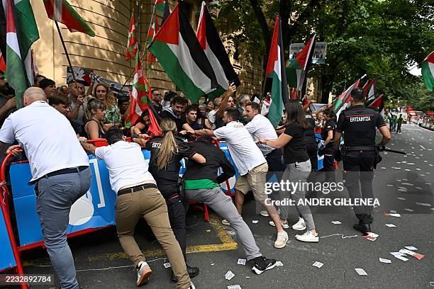 The Vuelta's staff members and Basque regional police 'Ertzaintza' officers hold barriers as pro-Palestinian protesters holding Palestinian and...