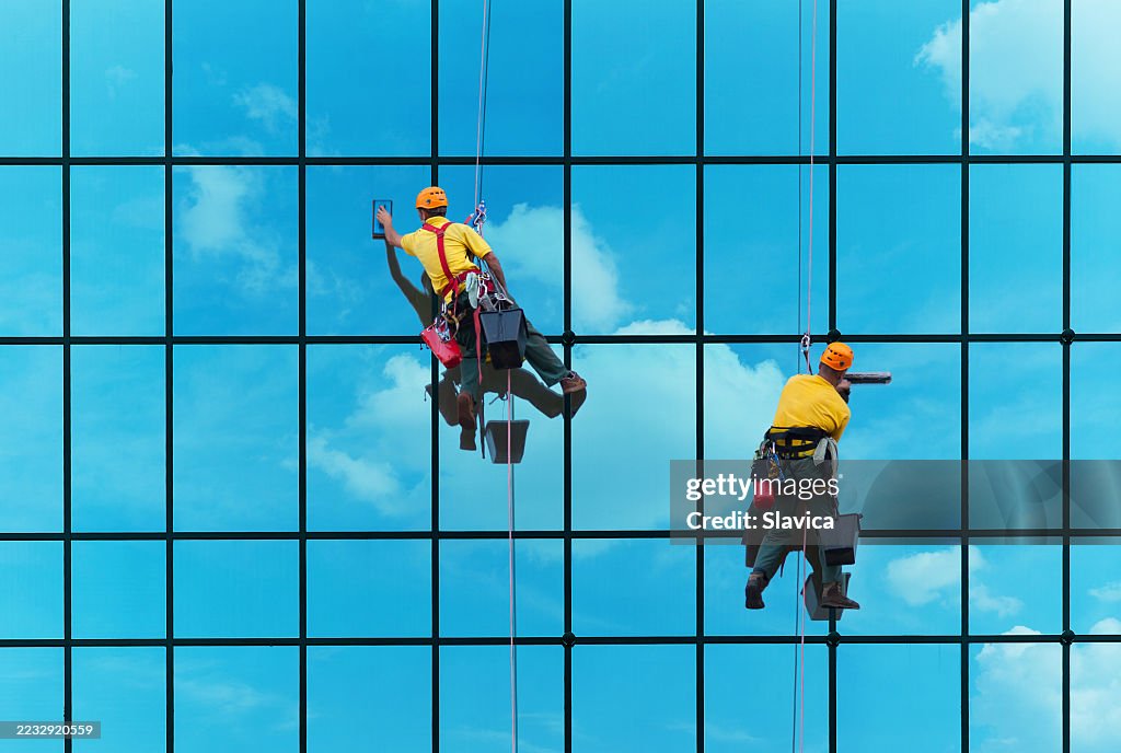 Two alpinists blue collar workers washing windows of the modern building on high altitude