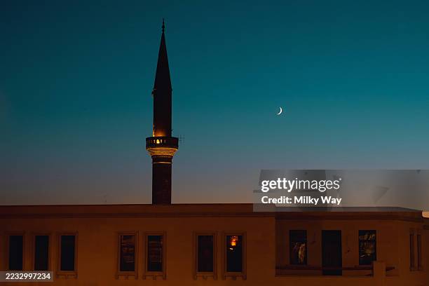 mosque minaret stands against a twilight sky with a crescent moon in the background. religion, spirituality and architecture concept. - crescent stock pictures, royalty-free photos & images