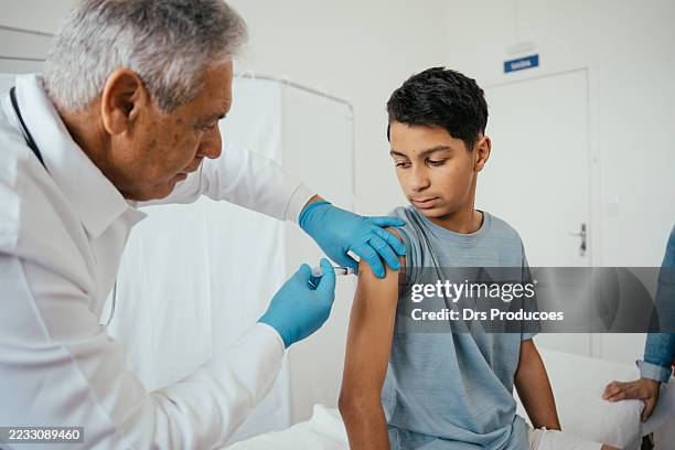doctor administering vaccine to teenager in doctor's office - covid 19 vaccine stock pictures, royalty-free photos & images