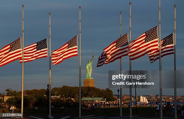 The sun sets on the Statue of Liberty in New York City as flags in the Liberty State Park flag plaza fly at half mast honoring the victims of the...