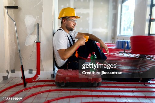 Construction worker taking a break, drinking coffee and using phone , during underfloor heating installation, Construction worker taking a break, drinking coffee and using phone , during underfloor heating installation,