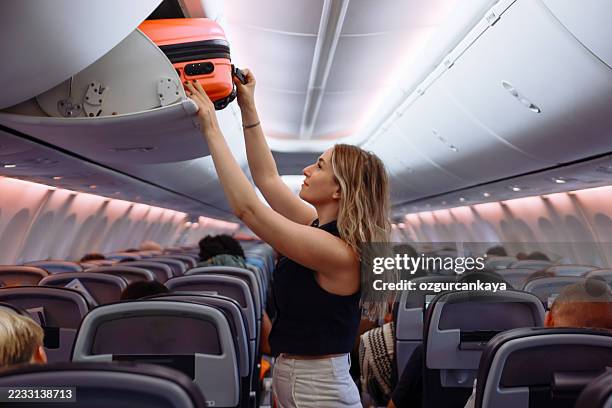 mujer poniendo equipaje de mano en casilleros sobre asientos de avión - taquilla recipiente fotografías e imágenes de stock