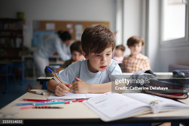 a child writing in his notebook in a classroom - grundschüler stock-fotos und bilder