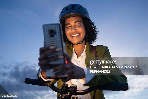 joven empresaria con casco, andando en bicicleta al atardecer y usando su teléfono inteligente para conectarse con otros mientras disfruta de la noche - ropa protectora deportiva fotografías e imágenes de stock