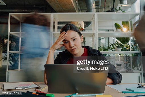 Jovem estressada trabalhando no laptop no escritório ocupado Jovem estressada trabalhando no laptop no escritório ocupado
