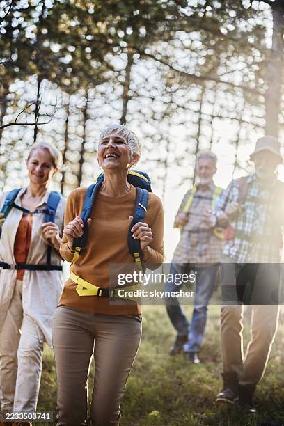 happy senior friends hiking through the woods. - buitensport stockfoto's en -beelden