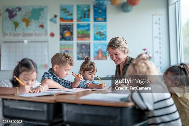 teacher assisting children during educational activity in a classroom setting - elementary school stock pictures, royalty-free photos & images