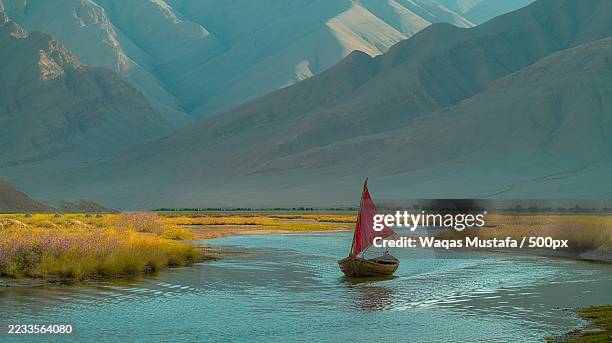 tranquil river with a red-sailed boat in a mountainous landscape,pakistan - calm water stock pictures, royalty-free photos & images