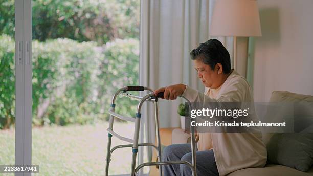 elderly asian woman getting up and trying to walk with a four-legged crutch at home. - mobility walker stock pictures, royalty-free photos & images